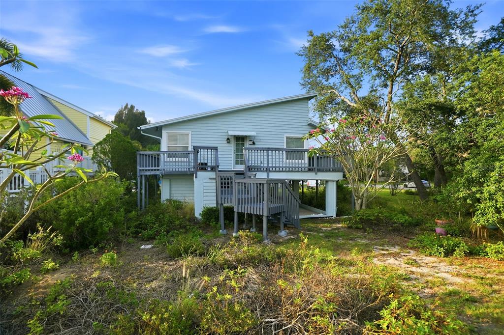 A light blue elevated house features a wooden deck, stairs, and surrounding lush landscaping — 110 GEORGIA AVE. AVENUE, CRYSTAL BEACH, FL
