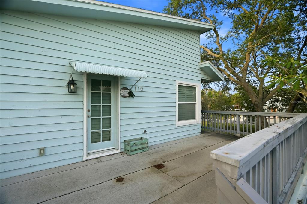 A light blue house exterior features a concrete balcony, a glass-paneled door, and wooden railings — 110 GEORGIA AVE. AVENUE, CRYSTAL BEACH, FL