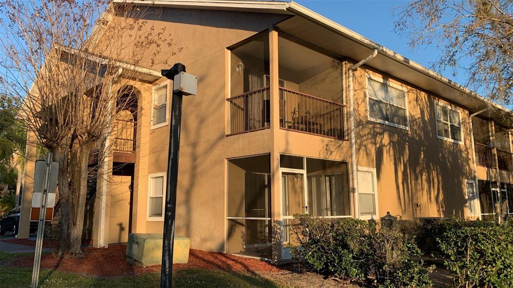 A two-story tan apartment building features screened-in balconies and patios with metal railings — 8834 CORAL PALMS COURT UNIT A, KISSIMMEE, FL