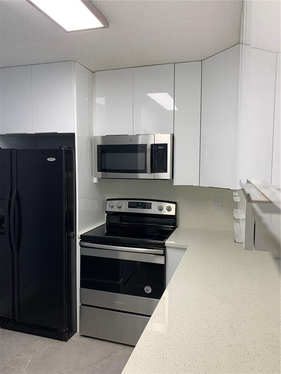 A kitchen features white cabinets, stainless steel appliances, a black refrigerator, and light-colored countertops — 8834 CORAL PALMS COURT UNIT A, KISSIMMEE, FL