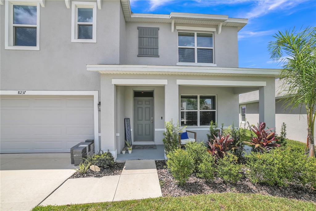 A two-story house exterior features a gray stucco facade, a garage, and a covered entryway — 8237 JUNING COVE, WESLEY CHAPEL, FL