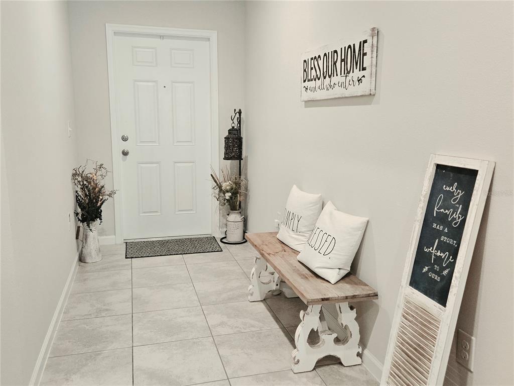 An entryway features a white front door, a wooden bench with pillows, and wall decor — 1121 LEXINGTON LANE, HAINES CITY, FL
