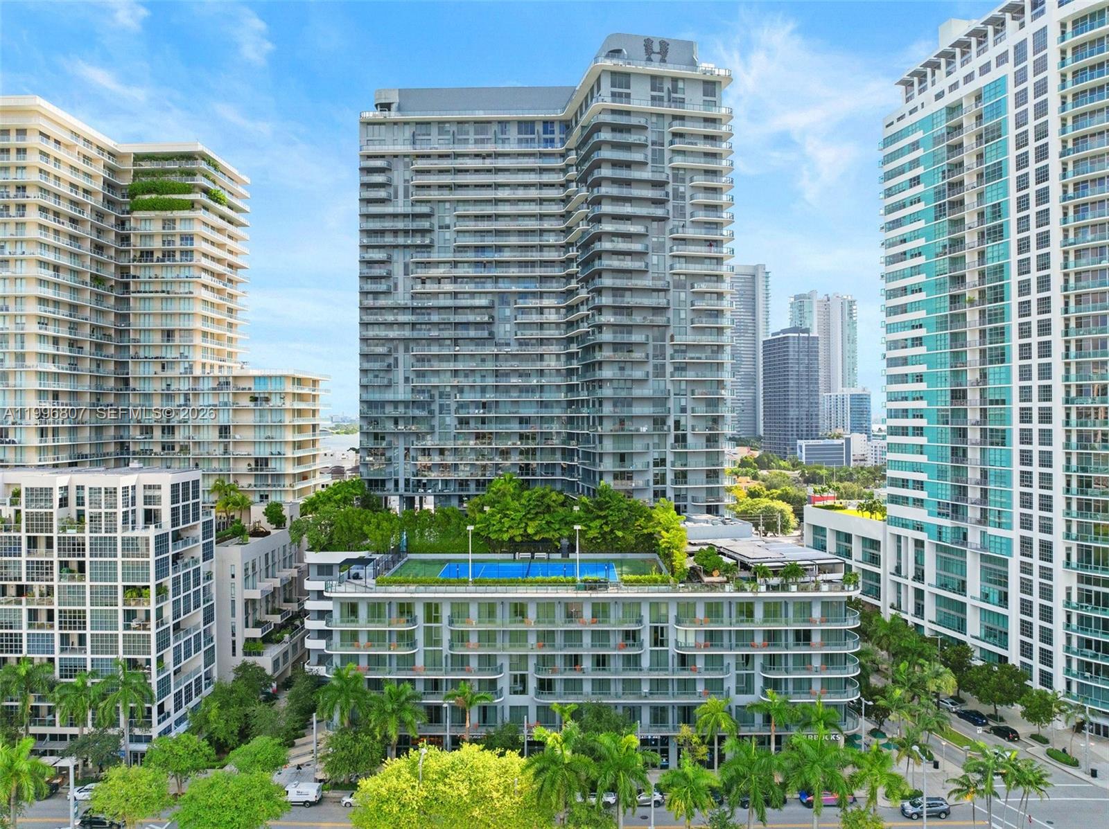 An exterior view of a tall residential building featuring a rooftop tennis court and balconies — 121 NE 34th St # 2314, Miami FL 33137, MIAMI, FL