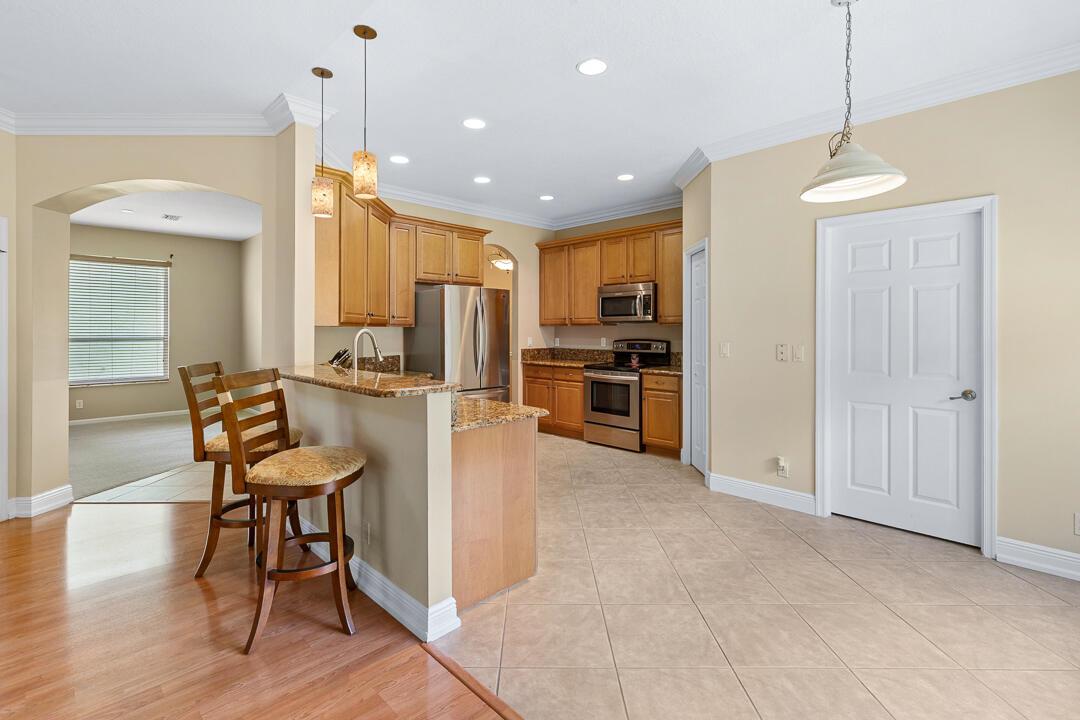 A kitchen features light wood cabinets, granite countertops, a breakfast bar, and tile flooring — 3516 NW Deer Oak Drive, Jensen Beach FL 34957, JENSEN BEACH, FL