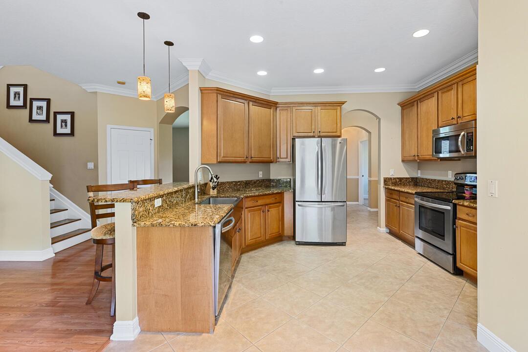 A kitchen features wood cabinets, granite countertops, stainless steel appliances, and tile flooring — 3516 NW Deer Oak Drive, Jensen Beach FL 34957, JENSEN BEACH, FL