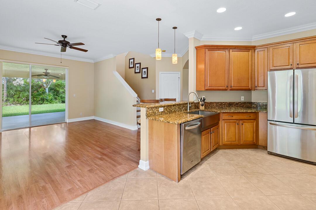 A kitchen with granite countertops and wood cabinets overlooks an adjacent living area with flooring — 3516 NW Deer Oak Drive, Jensen Beach FL 34957, JENSEN BEACH, FL
