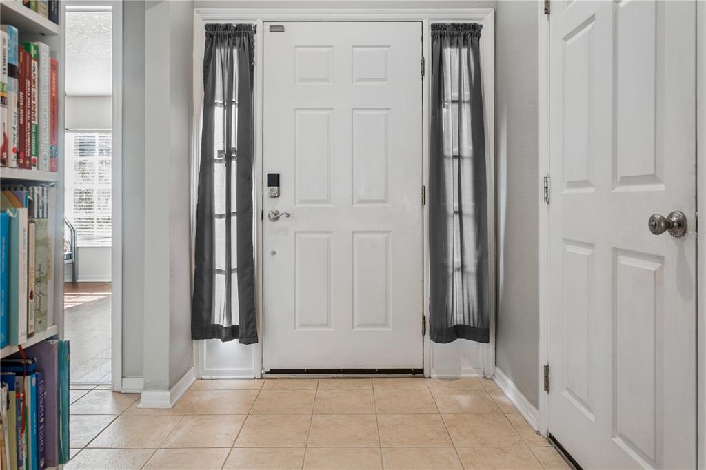 An entryway features a white front door with sidelights, tile flooring, and a built-in bookshelf — 5701 SWEET WILLIAM TERRACE, LAND O LAKES, FL