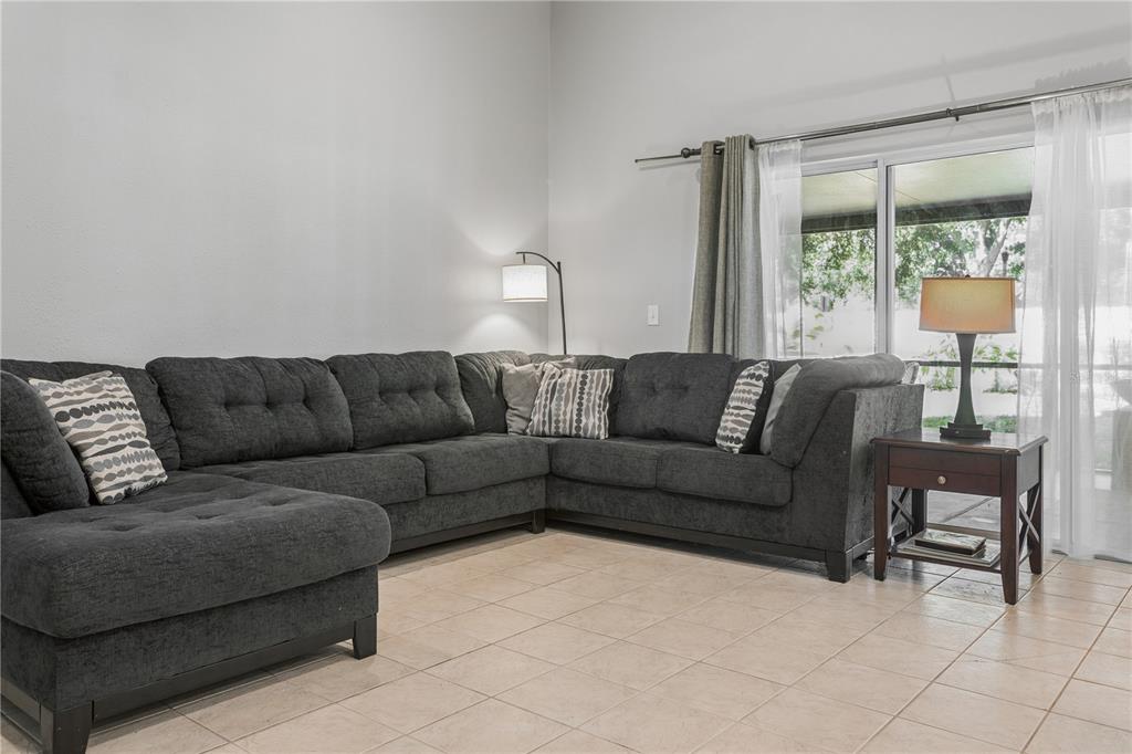 A living room features a large gray sectional sofa, a floor lamp, and sliding glass doors — 5701 SWEET WILLIAM TERRACE, LAND O LAKES, FL