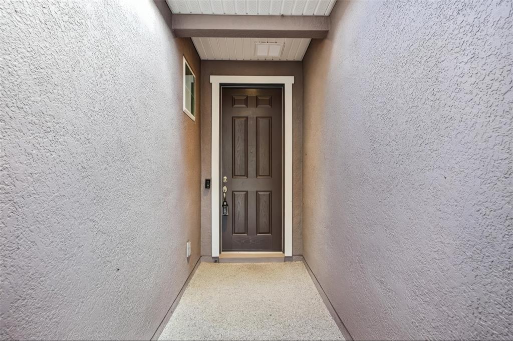 A narrow, covered entryway features a dark brown front door between two textured walls — 508 NARROW VIEW LANE, GROVELAND, FL