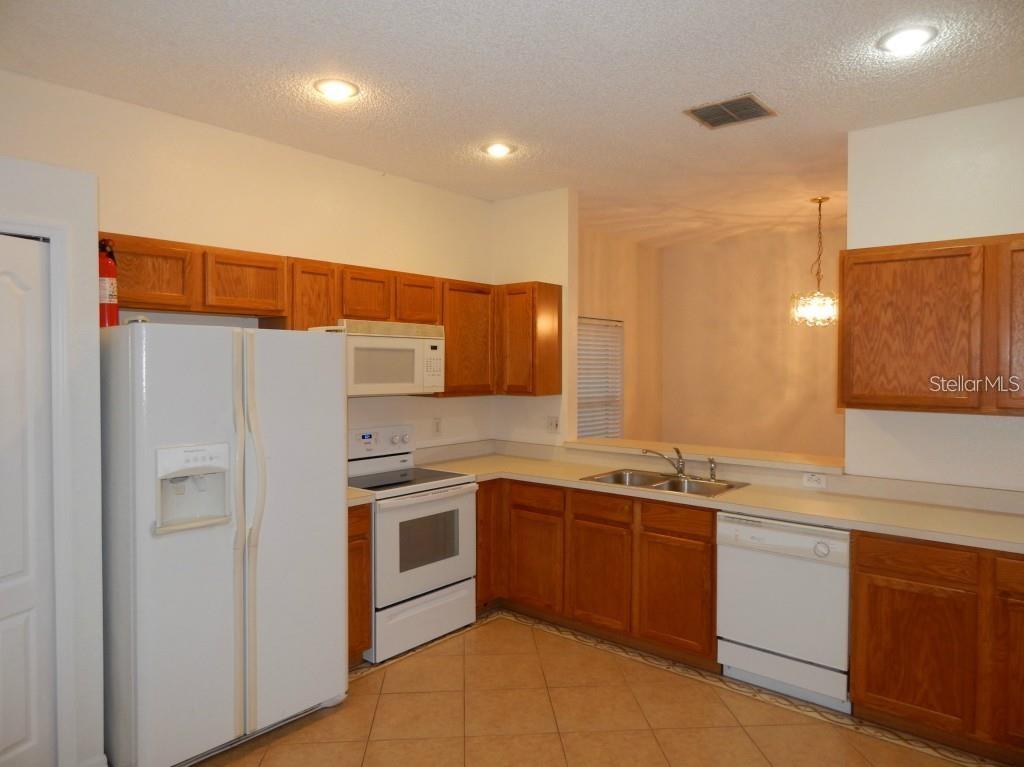 A kitchen with wood cabinets, white appliances, tile flooring, and a pass-through window — 4434 WATERSIDE POINTE CIRCLE, ORLANDO, FL