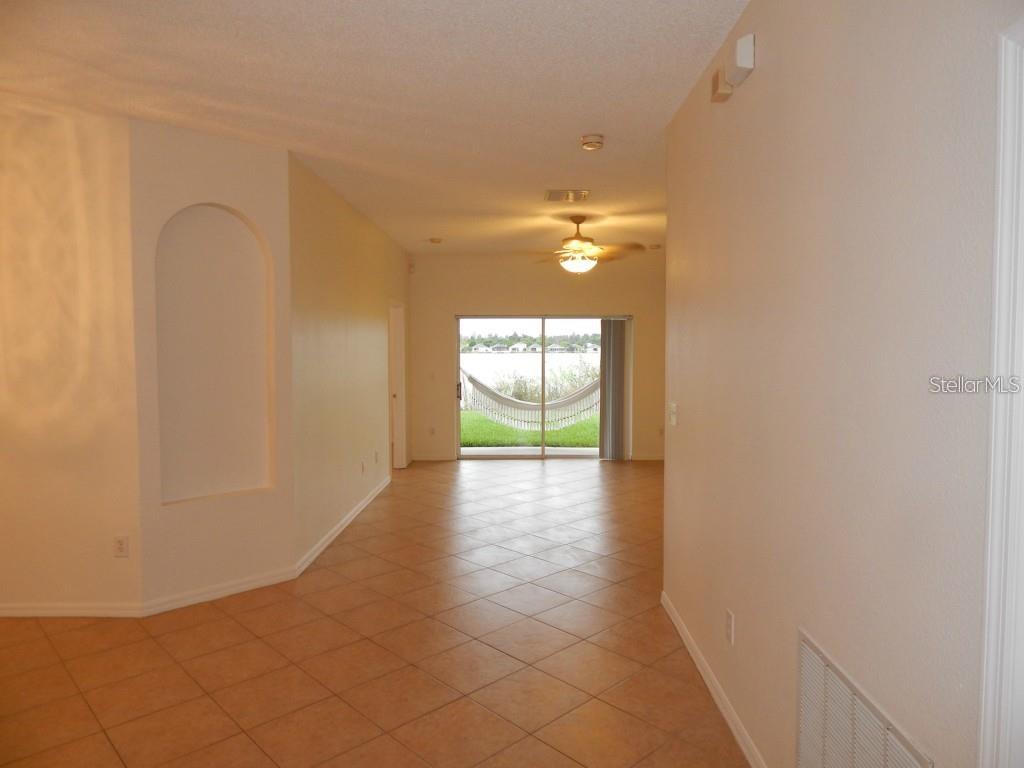 An empty room with tan tile floors, an arched wall niche, and a sliding glass door — 4434 WATERSIDE POINTE CIRCLE, ORLANDO, FL