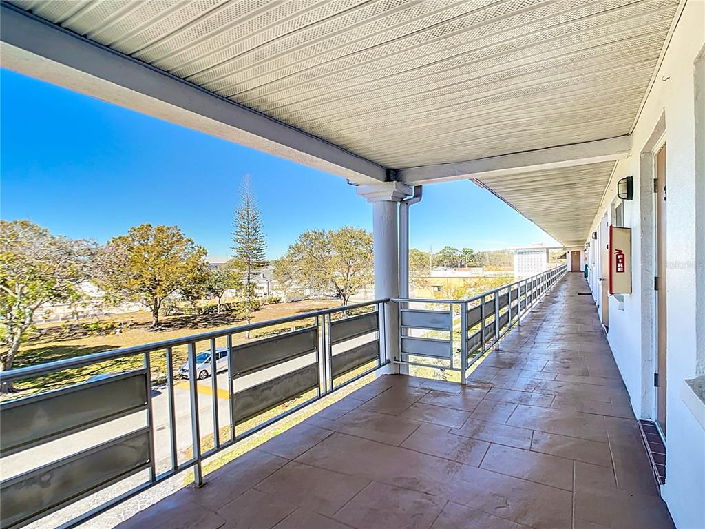 An outdoor covered walkway features a tiled floor, metal railings, and views of trees — 6015 19TH STREET N UNIT 308, ST PETERSBURG, FL