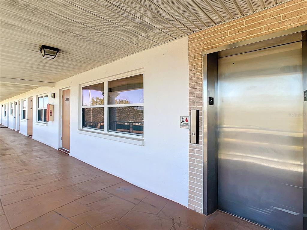 An outdoor apartment hallway features a metal elevator door, a window, and unit doors — 6015 19TH STREET N UNIT 308, ST PETERSBURG, FL