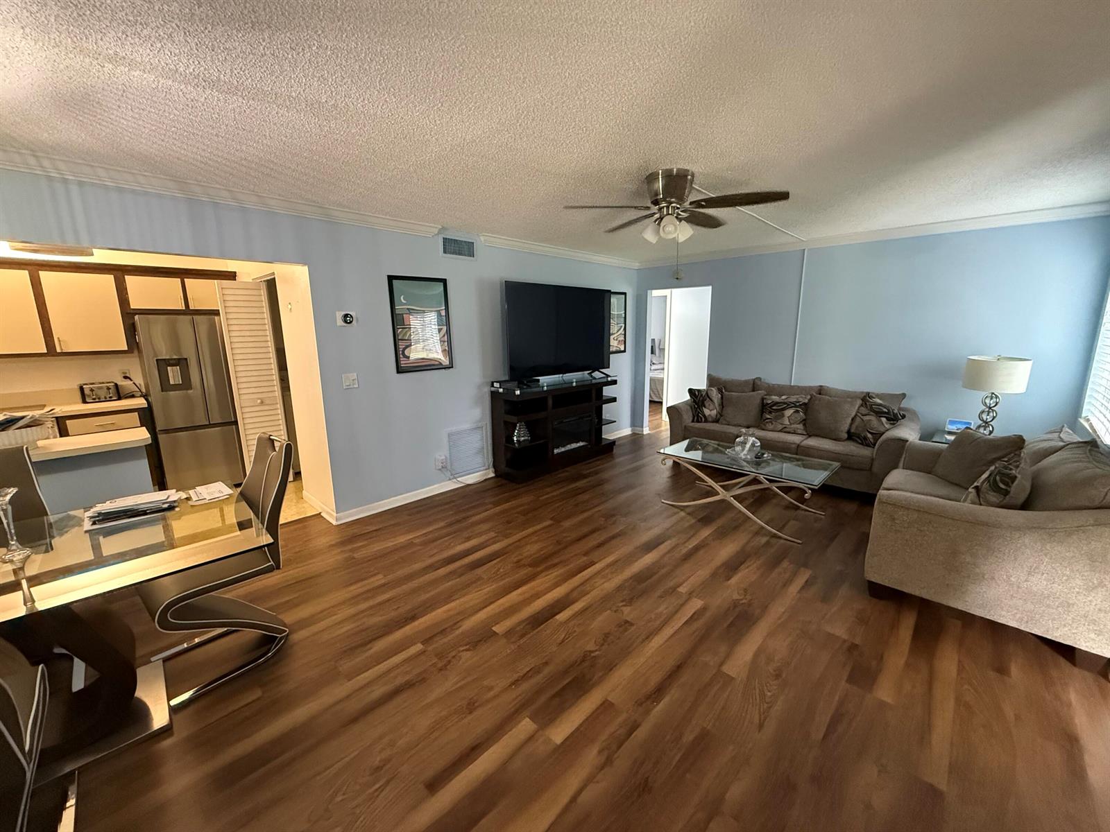 An open-concept living and dining area features light blue walls, wood-look flooring, and gray furniture — 301 Pine Ridge Circle # 1, FL 33463, FL