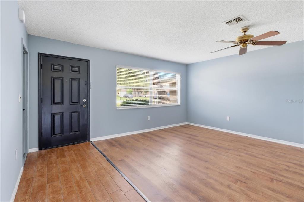 An empty living room features light blue walls, wood-look flooring, and a ceiling fan — 1289-1291 MARKHAM AVENUE, SPRING HILL, FL