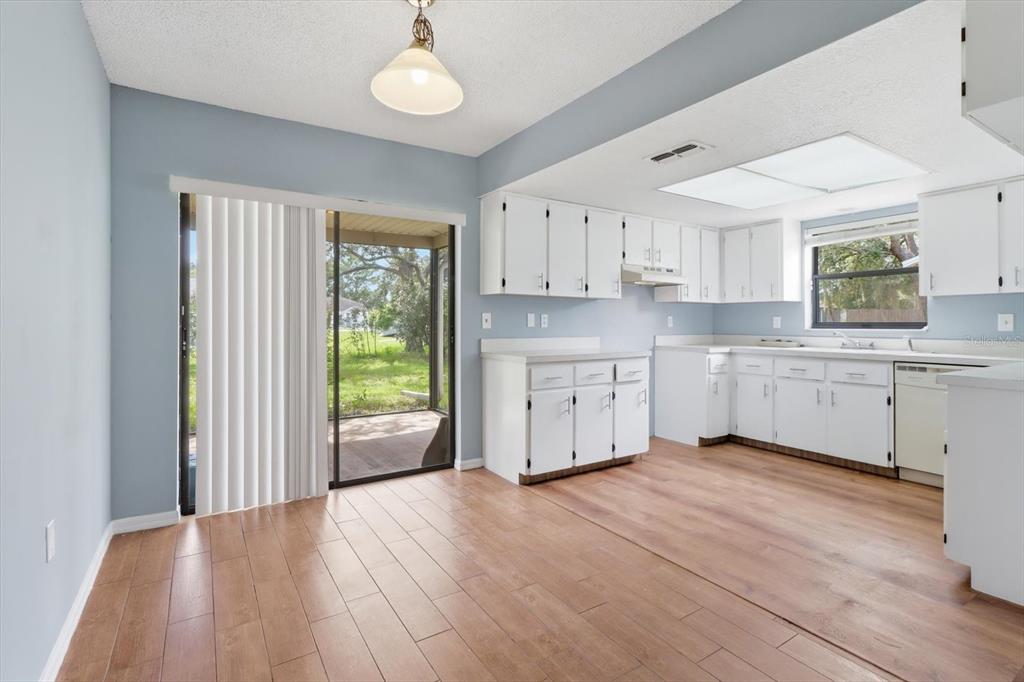 A kitchen and dining area with white cabinets, wood-look flooring, and a sliding glass door — 1289-1291 MARKHAM AVENUE, SPRING HILL, FL
