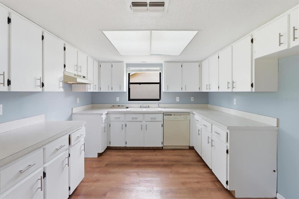 A kitchen features white cabinets, light countertops, a window, and wood-look flooring — 1289-1291 MARKHAM AVENUE, SPRING HILL, FL