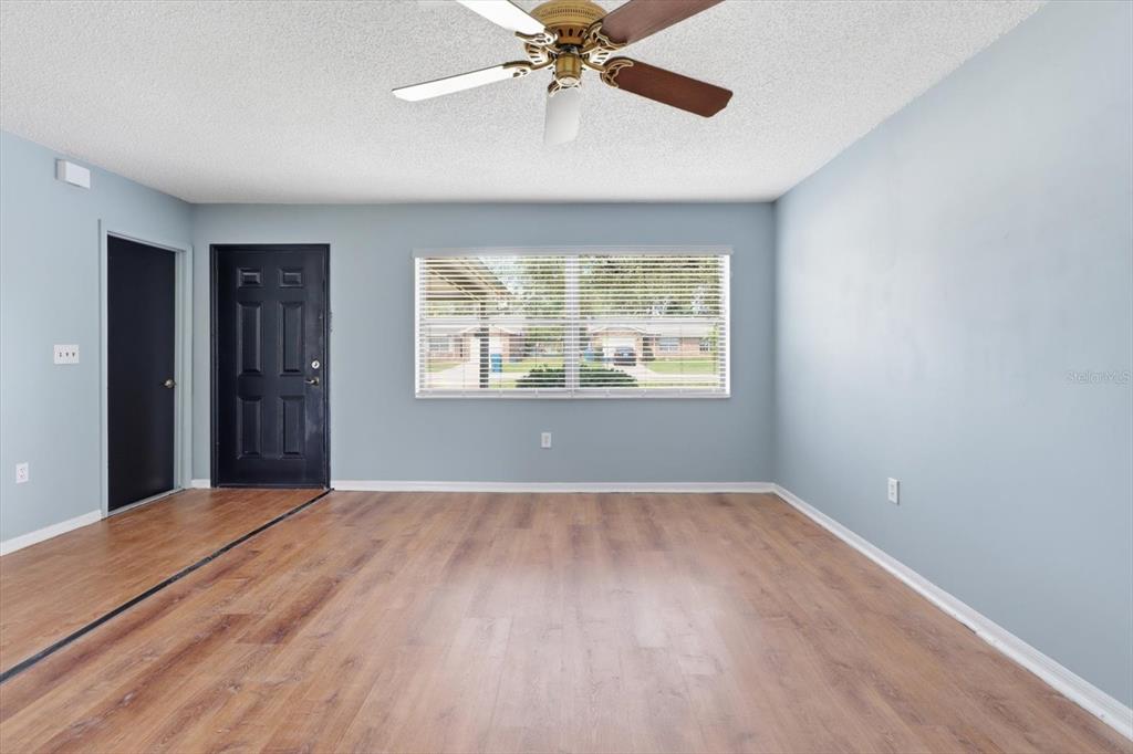 An empty room features light blue walls, wood-look flooring, a ceiling fan, and two doors — 1289-1291 MARKHAM AVENUE, SPRING HILL, FL