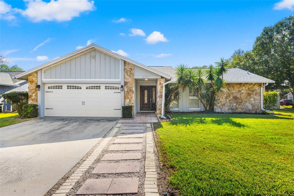 A single-story house features a stone facade, a two-car garage, and a paved walkway — 6701 LEEWARD ISLE WAY, TAMPA, FL