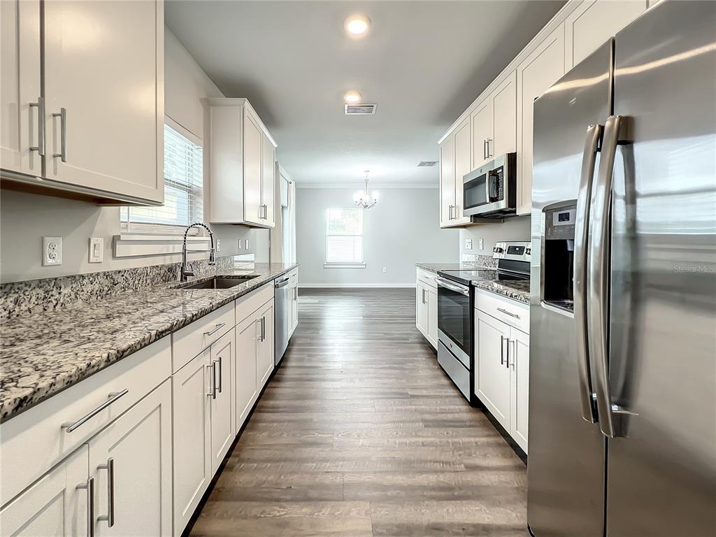 A galley kitchen features white cabinets, granite countertops, stainless steel appliances, and wood-look flooring — 3715 W WISCONSIN AVENUE UNIT 3, TAMPA, FL