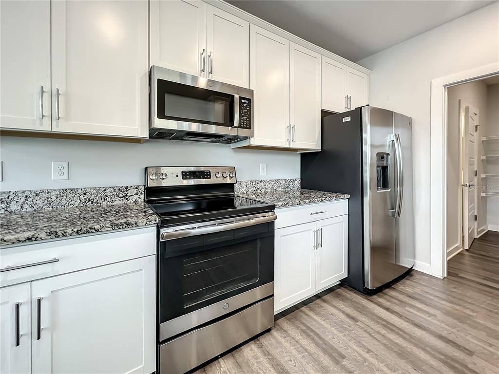 A kitchen features white cabinets, granite countertops, stainless steel appliances, and wood-look flooring — 3715 W WISCONSIN AVENUE UNIT 3, TAMPA, FL