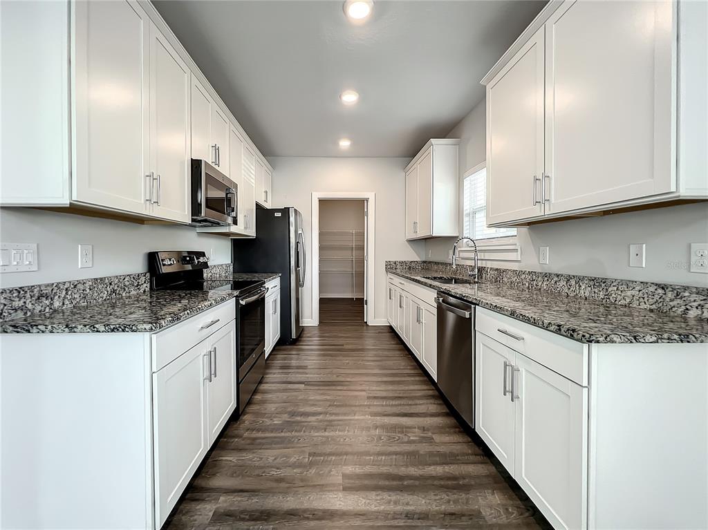 A galley kitchen features white cabinets, granite countertops, stainless steel appliances, and wood-look flooring — 3715 W WISCONSIN AVENUE UNIT 3, TAMPA, FL