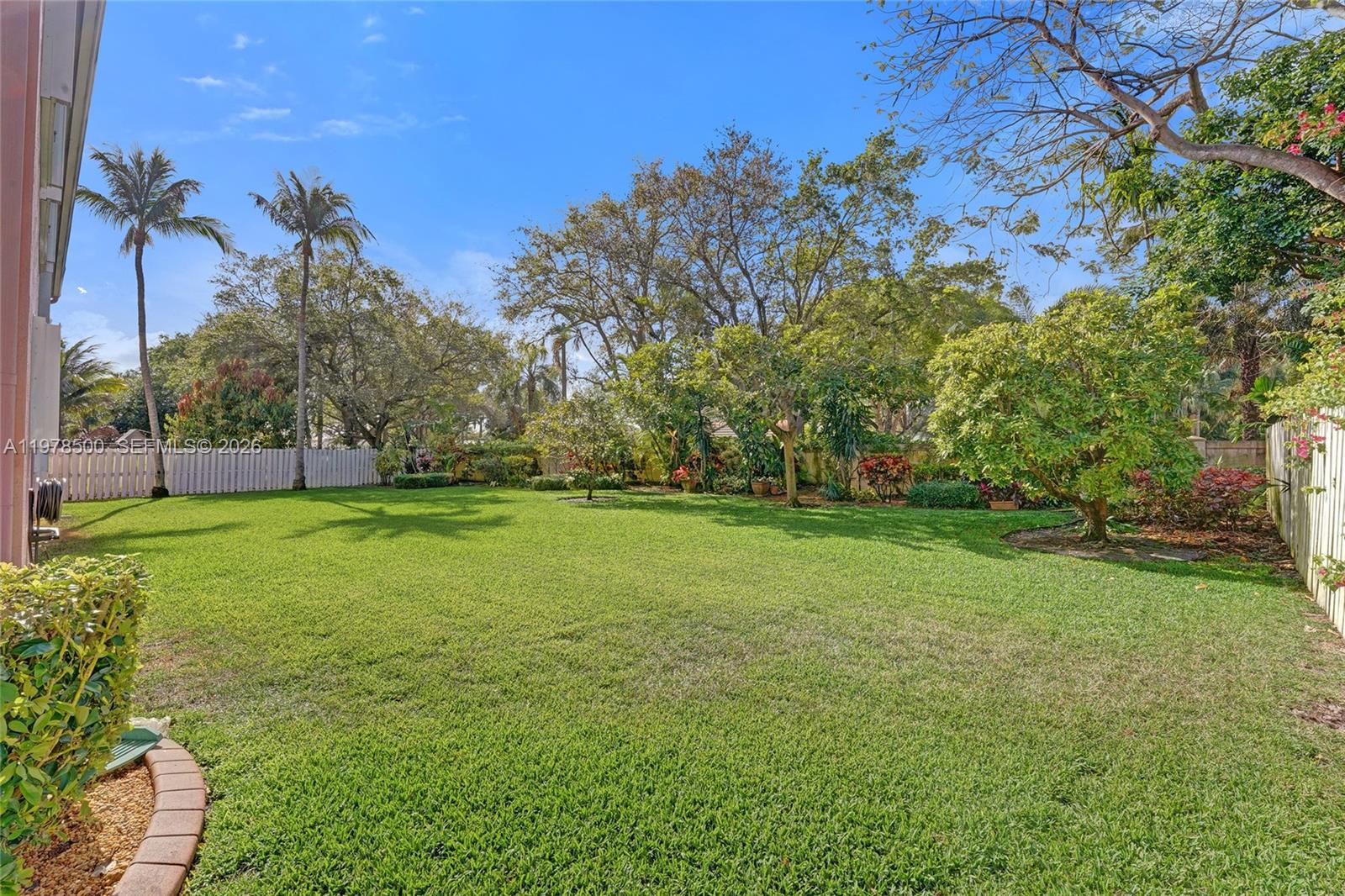 A spacious backyard features a manicured lawn, various trees, and a white privacy fence — 14686 SW 35th Ct, Miramar FL 33027, MIRAMAR, FL