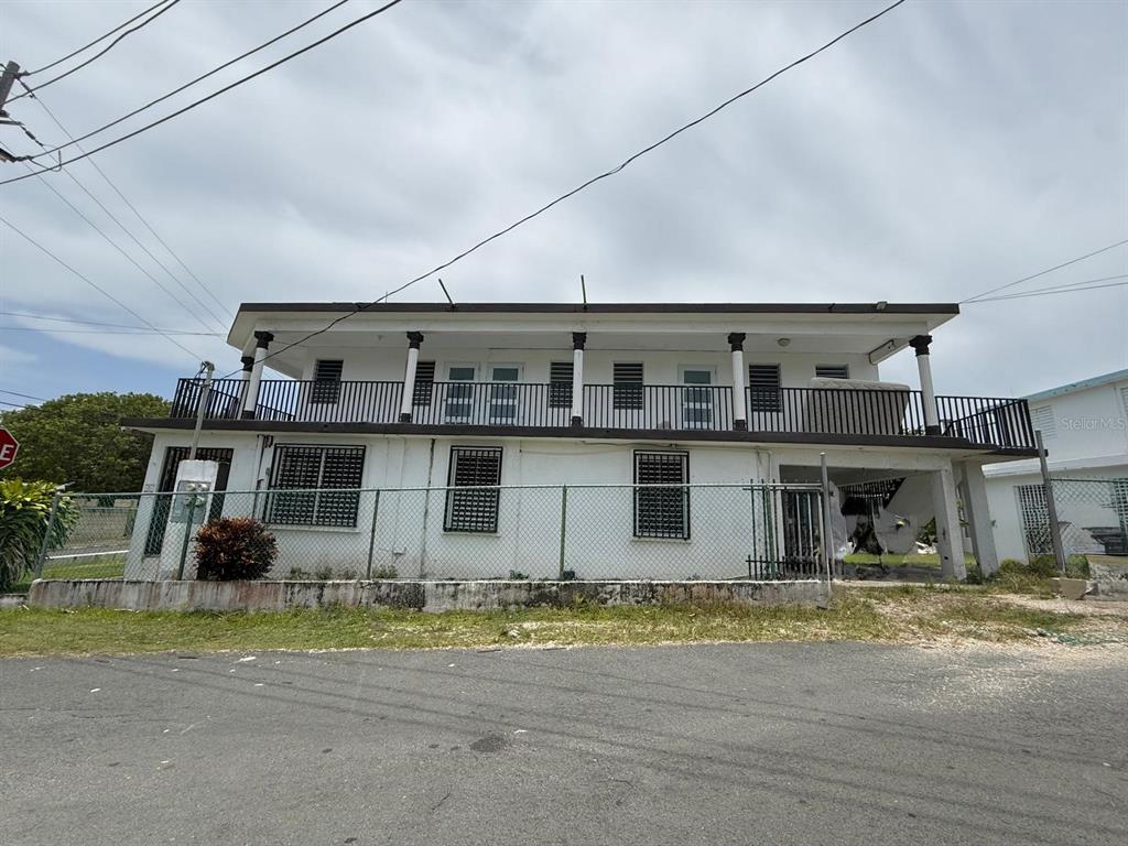 A two-story white building features a second-floor balcony with black railings and a chain-link fence — 53 P35 CALLE SATURNO 53, COM. SANDIN UNIT 2, VEGA BAJA, PR