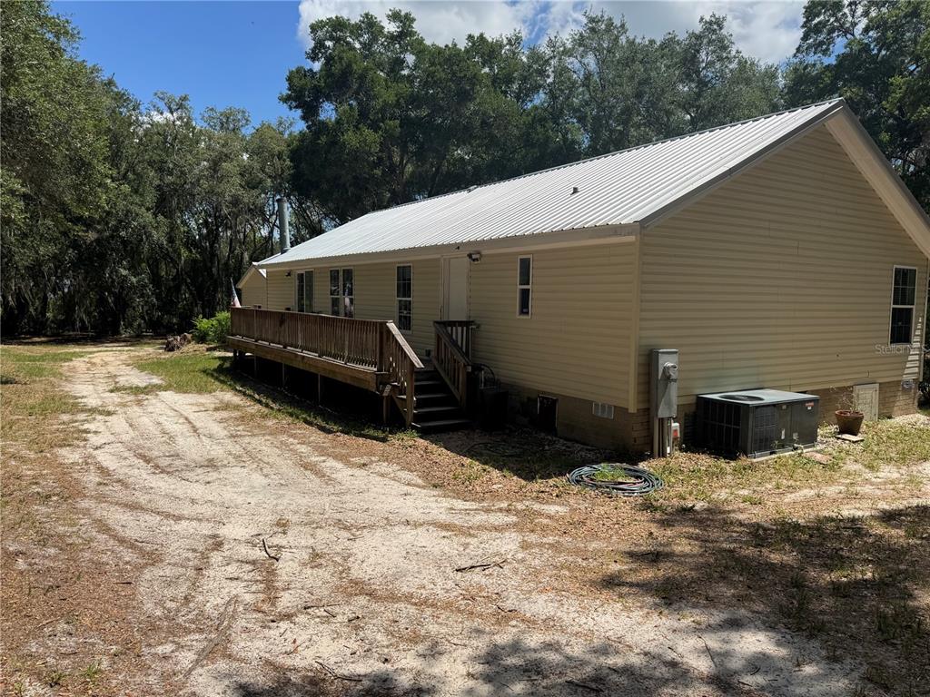 A tan house with a metal roof and a wooden deck sits on a dirt lot — 10645 SE 145TH STREET, SUMMERFIELD, FL