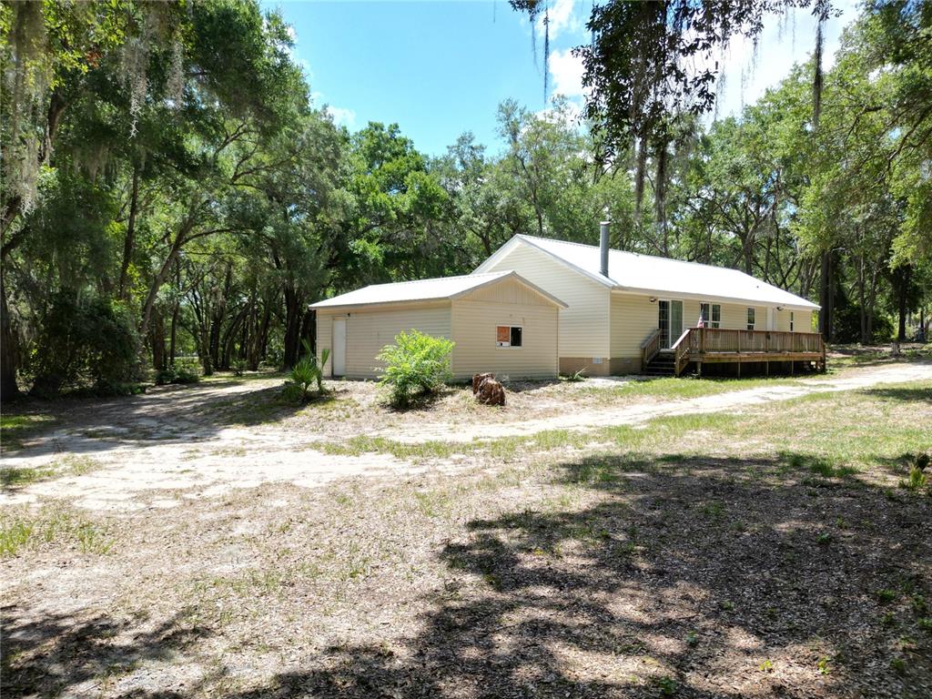 A light-colored house with a metal roof and a wooden deck sits among trees — 10645 SE 145TH STREET, SUMMERFIELD, FL