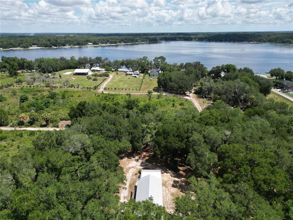 An aerial view shows a house nestled in trees with a large field and lake beyond — 10645 SE 145TH STREET, SUMMERFIELD, FL