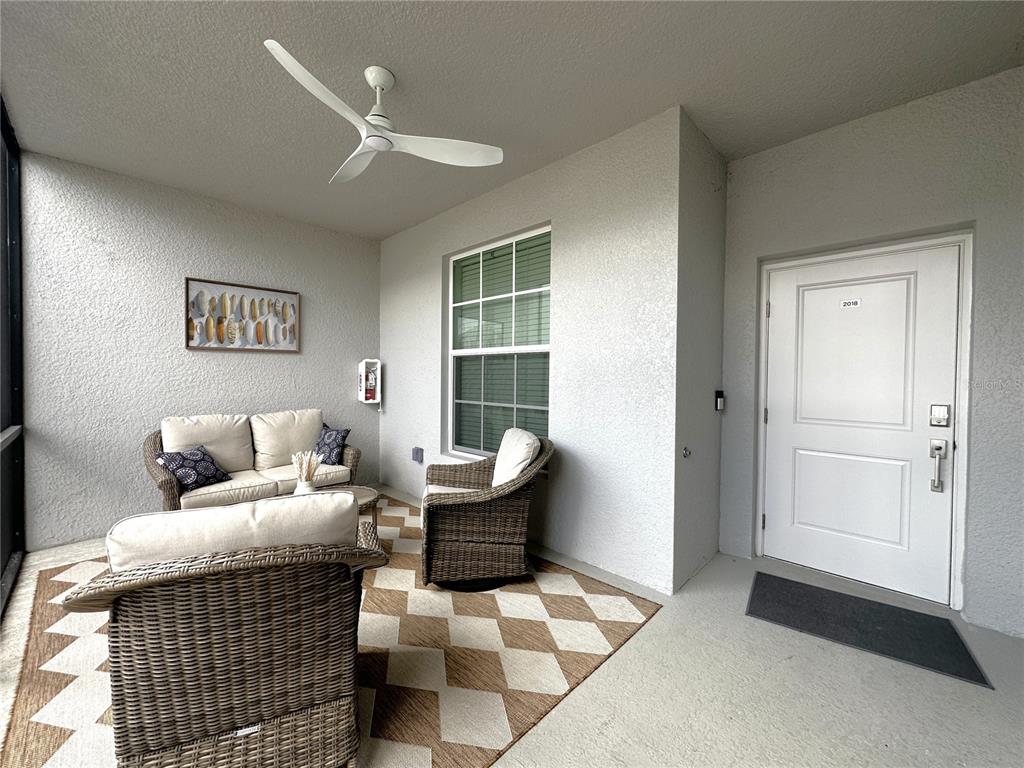A covered patio features wicker furniture, a patterned rug, a ceiling fan, and a white door — 14221 HERITAGE LANDING BOULEVARD UNIT 2018, PUNTA GORDA, FL