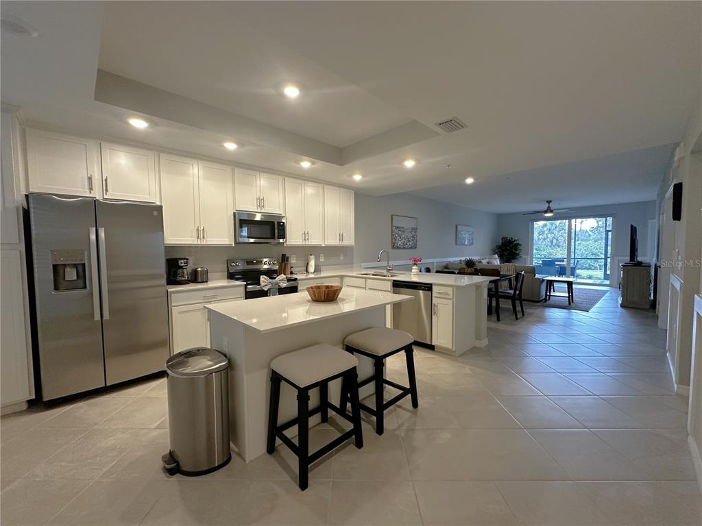 A modern kitchen with white cabinets, stainless steel appliances, and an island with two stools — 14221 HERITAGE LANDING BOULEVARD UNIT 2018, PUNTA GORDA, FL