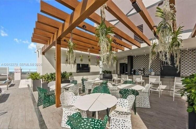 An outdoor rooftop patio features a wooden pergola, hanging plants, and white patterned patio furniture — 1010 Brickell Ave # 1910, Miami FL 33131, MIAMI, FL