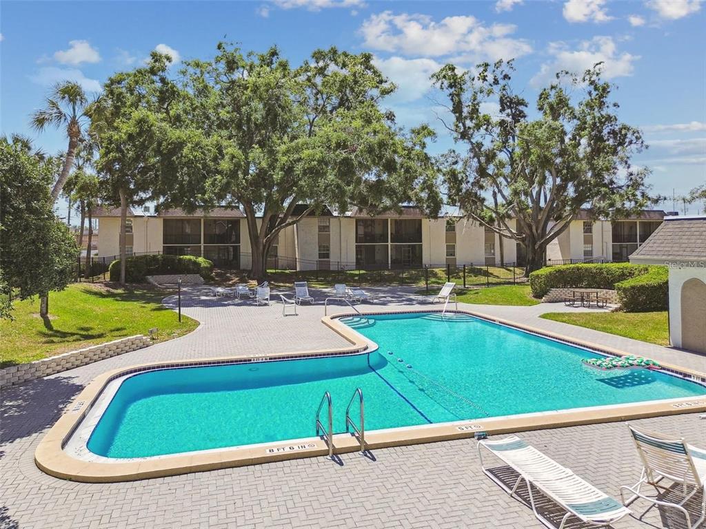 An outdoor swimming pool with a brick deck and lounge chairs sits before apartment buildings — 122 N KINGS AVENUE UNIT 101, BRANDON, FL