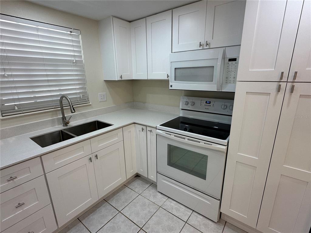 A kitchen features white cabinets, stainless steel appliances, a double sink, and tiled flooring — 122 N KINGS AVENUE UNIT 101, BRANDON, FL