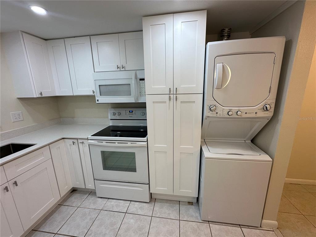 A kitchen features white cabinets, a stove, a microwave, and a stacked washer and dryer — 122 N KINGS AVENUE UNIT 101, BRANDON, FL