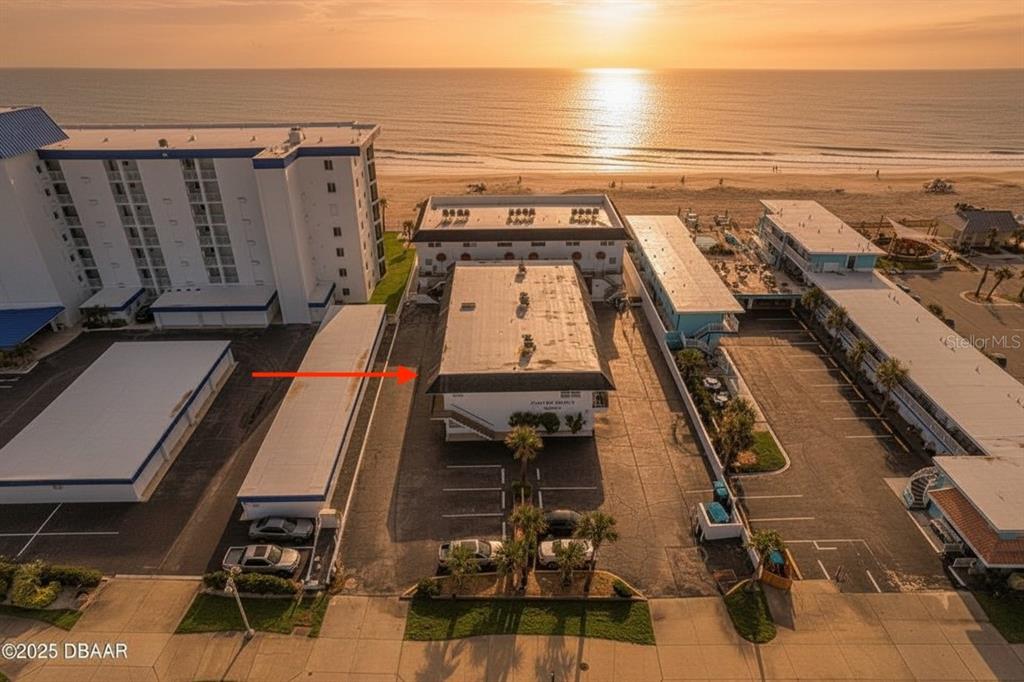 An aerial view shows a multi-story building complex situated along a sandy beach at sunset — 3615 S ATLANTIC AVENUE UNIT 211, DAYTONA BEACH, FL