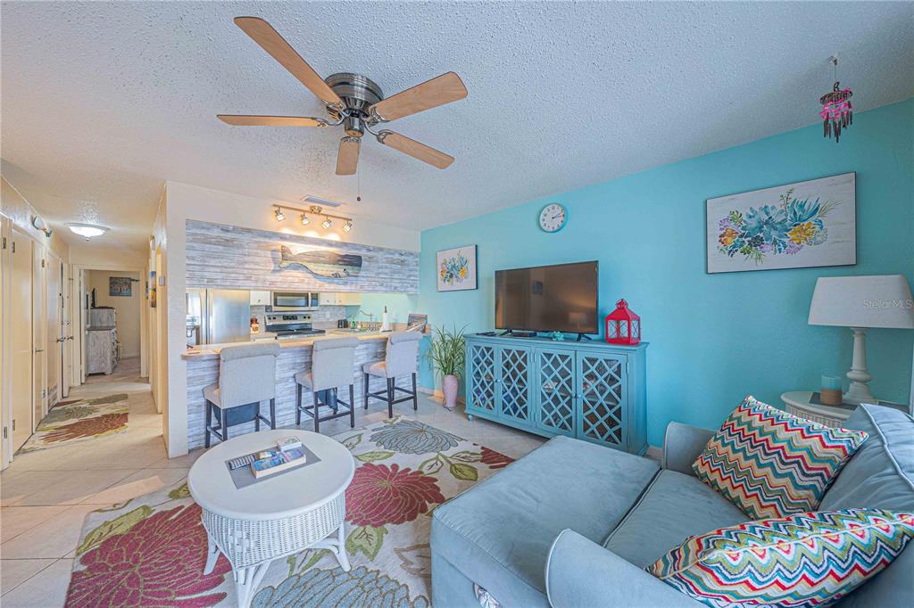 A living room with a light blue wall, a television console, and a kitchen breakfast bar — 3615 S ATLANTIC AVENUE UNIT 211, DAYTONA BEACH, FL