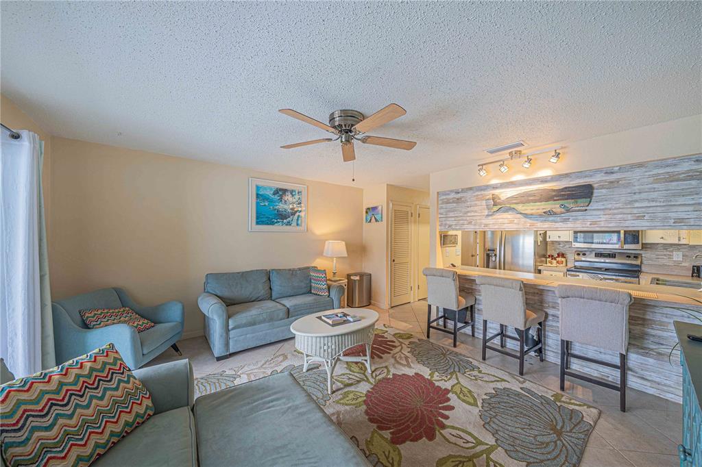 A living room with a sofa, armchairs, and a breakfast bar overlooking the kitchen — 3615 S ATLANTIC AVENUE UNIT 211, DAYTONA BEACH, FL