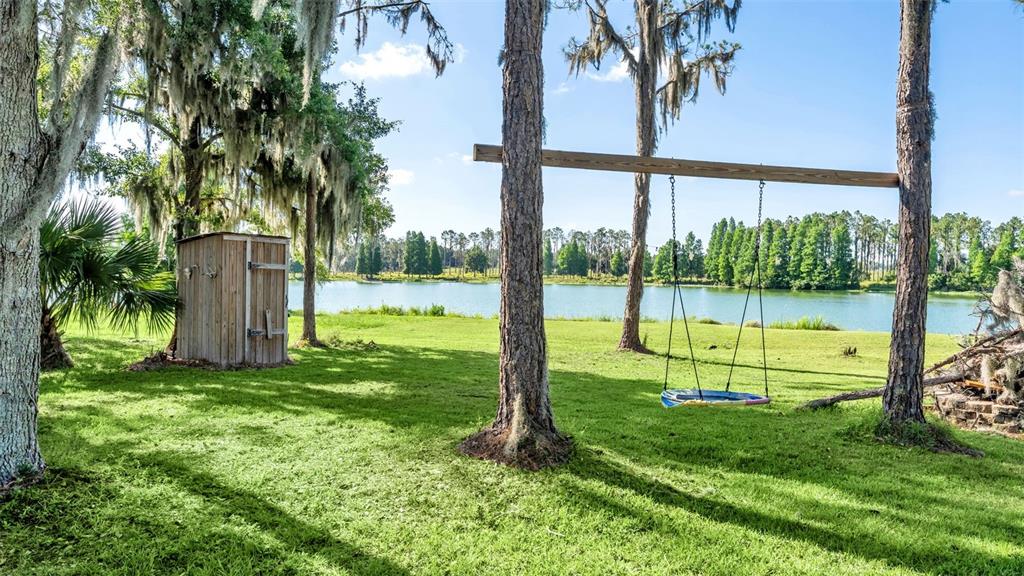 A wooden shed and a circular swing stand on a grassy lawn beside a lake — 1044 TIMBERS DRIVE, FORT MEADE, FL