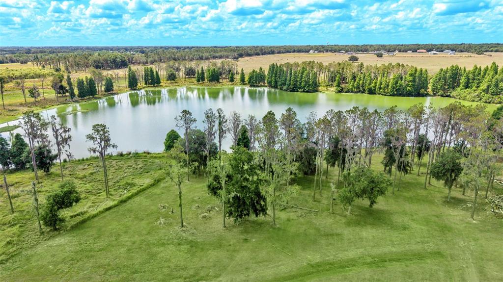 An aerial view of a grassy field with scattered trees bordering a large, calm lake — 1044 TIMBERS DRIVE, FORT MEADE, FL
