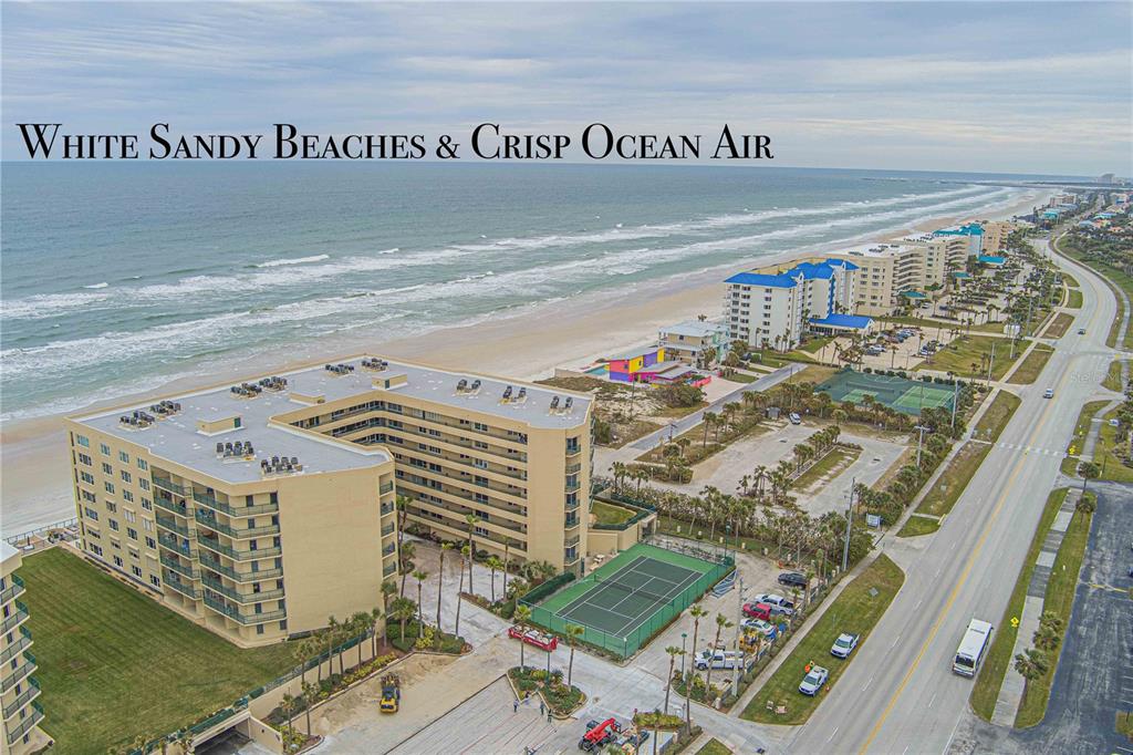 An aerial view shows a large beachfront apartment complex with a tennis court and parking — 4575 S ATLANTIC AVENUE UNIT 6209, PONCE INLET, FL