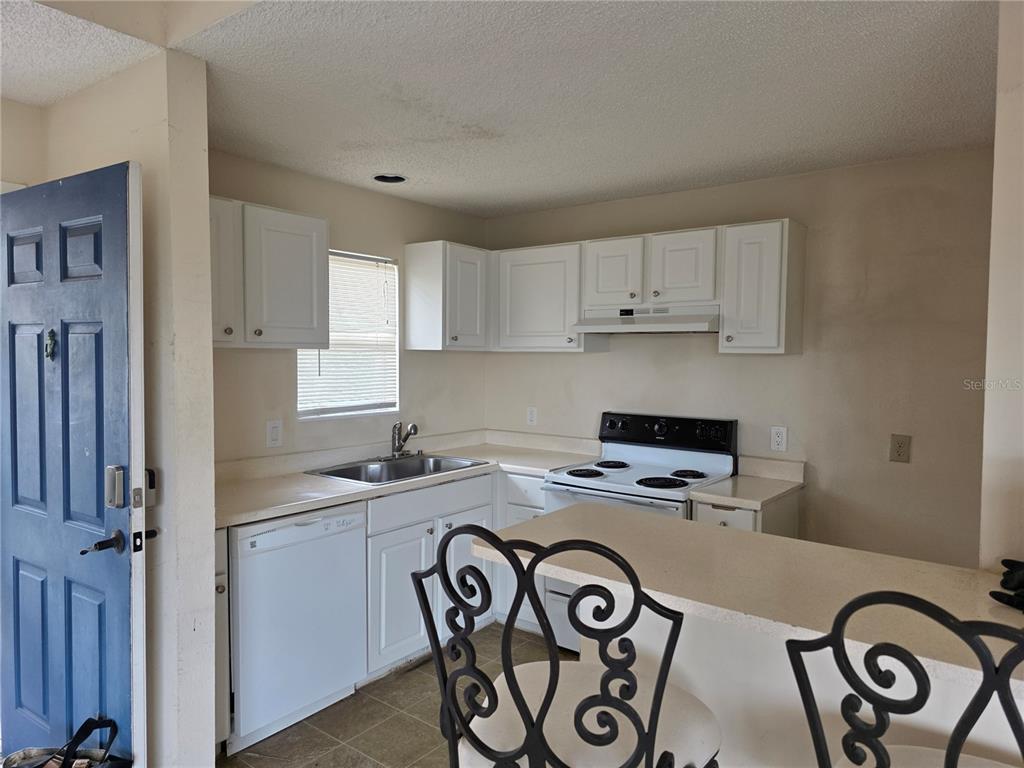 A kitchen features white cabinets, white appliances, a sink, and a breakfast bar with stools — 115 112TH AVENUE NE UNIT 1024, ST PETERSBURG, FL