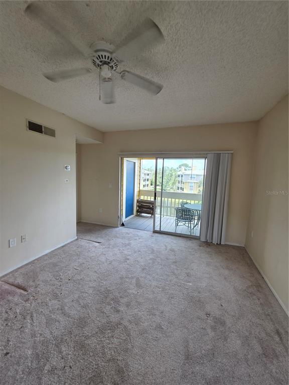 An empty carpeted room features a ceiling fan, beige walls, and a sliding glass balcony door — 115 112TH AVENUE NE UNIT 1024, ST PETERSBURG, FL