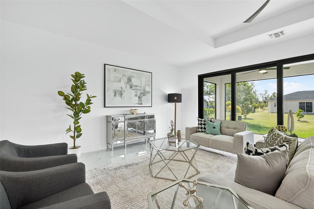 A modern living room features a mirrored console, gray armchairs, and large sliding glass doors — 4202 14TH STREET SW, LEHIGH ACRES, FL