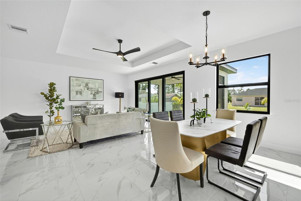 A bright open-concept living and dining area features white marble floors and a tray ceiling — 4202 14TH STREET SW, LEHIGH ACRES, FL