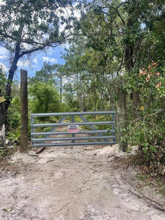 A metal gate blocks a dirt path between two wooden posts in a wooded area — 10128 S SUNCOAST BOULEVARD, HOMOSASSA, FL