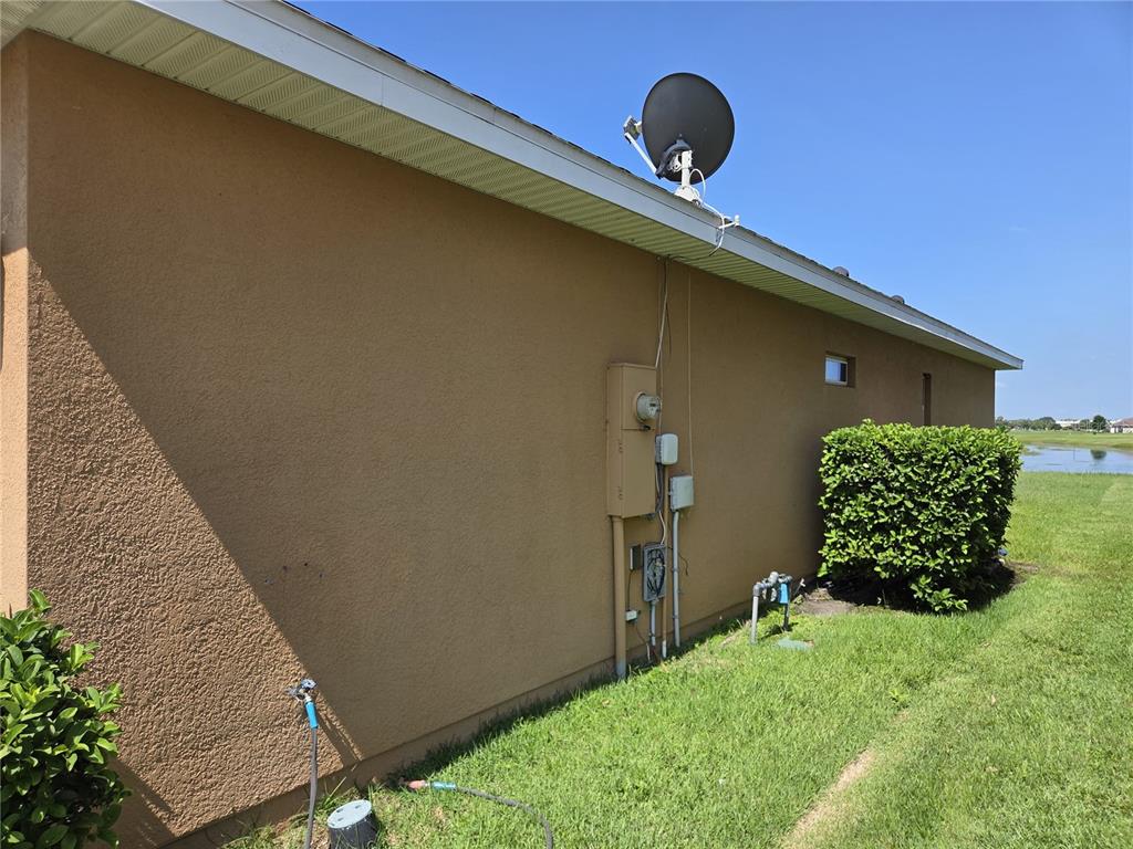 The exterior side wall of a house features a satellite dish, electrical meter, and landscaping — 2280 SHEBOYGAN PLACE, KISSIMMEE, FL