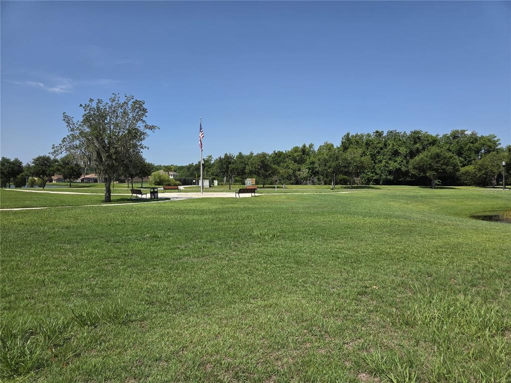 A grassy park features a flagpole, several benches, and a paved path under a blue sky — 2280 SHEBOYGAN PLACE, KISSIMMEE, FL